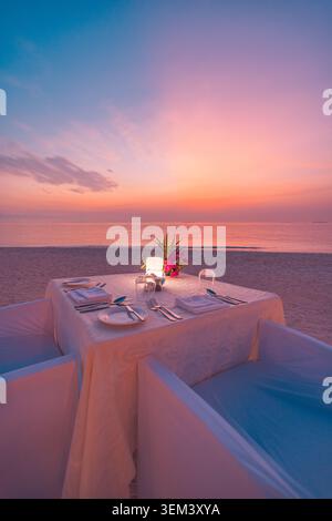 Candlelit romantic beach dinner table for two at tropical sunset. Ocean view pink sky honeymoon. Luxury summer travel vacation getaway celebration Stock Photo