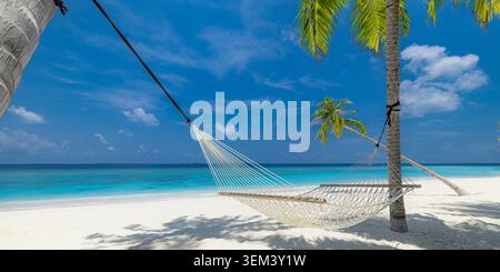 Empty beach hammock swaying between palms above calm turquoise ocean lagoon. Sunny tropical island white sand. Summer holiday travel vacation paradise Stock Photo