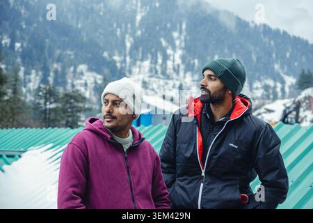 Two young men in warm winter clothing standing outdoors against a backdrop of snowy mountains in Kashmir, India. Stock Photo