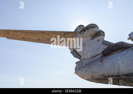Low-angle close-up of a weathered abandoned ekranoplan, a wing-in-ground effect craft, showing wing and fuselage details against a clear blue sky Stock Photo