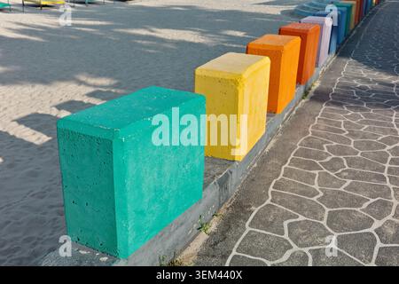 Colorful painted concrete blocks in teal, yellow, orange, and purple lining a beach promenade beside white sand and stone pathway, Gangneung Stock Photo