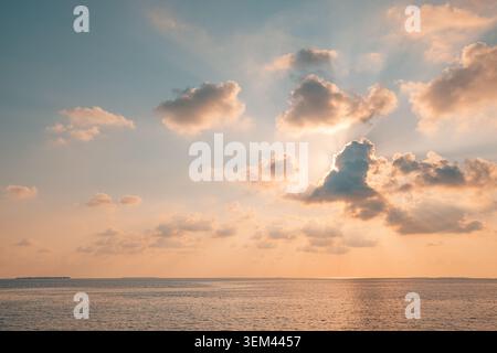 Dramatic cloudscape glowing over calm tropical ocean horizon. Soft sunlight breaking through white clouds. Scenic seascape sky nature design Stock Photo