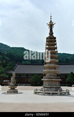 Nine-story granite Buddhist pagoda with gold finial and Bodhisattva sculpture in sandy courtyard of a Korean temple, Gangwon Province, South Korea. Stock Photo