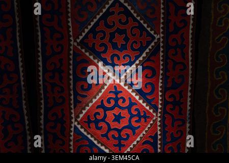 Bishkek, Kyrgyzstan - February 25, 2025: Close-up of traditional Kyrgyz shyrdak felt carpet with red and blue geometric ornament, photographed inside Stock Photo