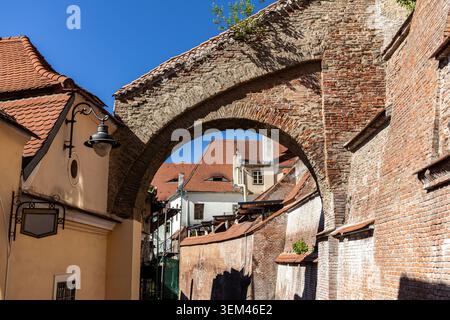 An outdoor low-angle view of a historic weathered red brick archway fortification bridge connecting old town medieval residential buildings under a br Stock Photo