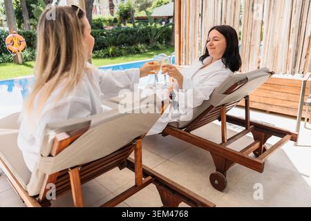 Friends in bathrobes toasting by the pool Stock Photo