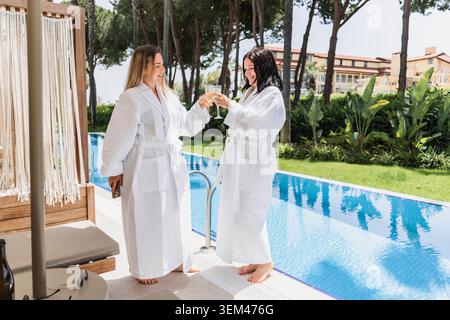 Happy women in bathrobes toasting by a pool Stock Photo