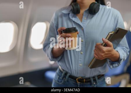 Asian woman holding coffee and tablet in airplane for travel Stock Photo
