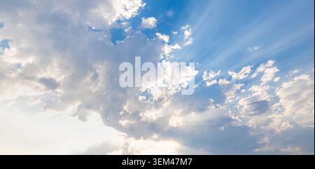 Sunlight rays streaming through white clouds across wide blue sky at daytime. Bright sunbeams cloudscape. Sky clouds nature heaven copy space Stock Photo