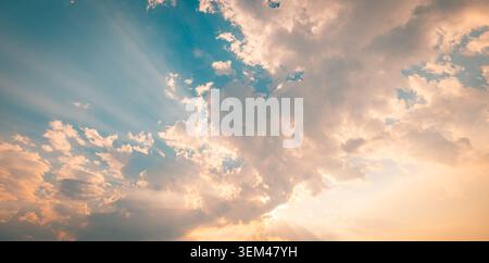 Dramatic sunset sky with golden sun rays breaking through clouds at dusk. Warm cloudscape sunbeams glow. Sky clouds nature heaven copy space Stock Photo