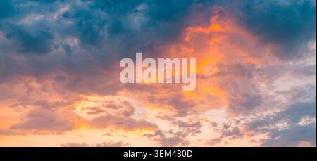 Fiery orange sunset glow burning through dark moody storm clouds at dusk. Bold cloudscape natural backdrop. Dramatic heaven background copy space Stock Photo