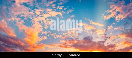 Dramatic sunset sky vivid orange pink clouds glowing sunbeams twilight panorama horizon. Summer evening cloudscape landscape. Wall art wallpaper art Stock Photo