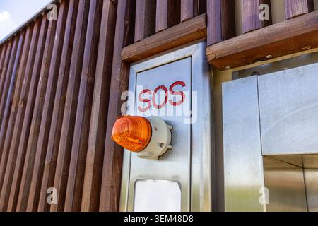 A close-up view of an outdoor emergency SOS system with a prominent orange push button and bold red text, installed on a stainless steel automated toi Stock Photo