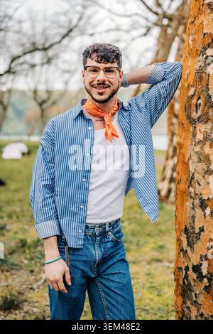 Young man smiling and leaning on tree outdoors Stock Photo