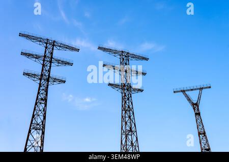 Three large Soviet-era steel transmission pylons without cables silhouetted against a clear blue sky on the Baku waterfront. Baku, Azerbaijan. Stock Photo
