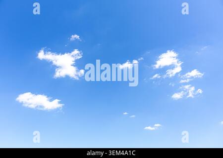 A low angle background shot of a beautiful deep blue sky populated with a few small, scattered white clouds during a clear sunny day. Stock Photo