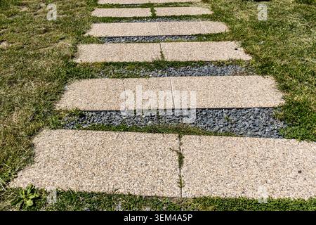 A detailed close-up shot of a modern outdoor pedestrian path consisting of parallel concrete paving slabs embedded in gray gravel with small patches o Stock Photo