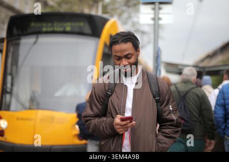 Young Black man looking at his smartphone at a tram stop Stock Photo