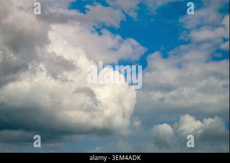 Fluffy white clouds against a bright blue sky with sections of gray Stock Photo
