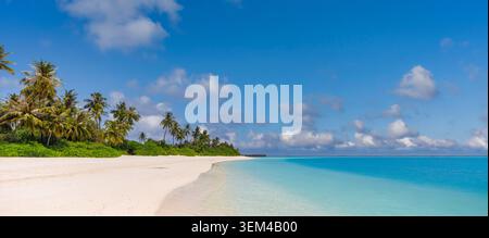 Wide tropical beach panorama, lush palm island curving along turquoise lagoon, white sand under blue sky with clouds, untouched paradise summer coast Stock Photo