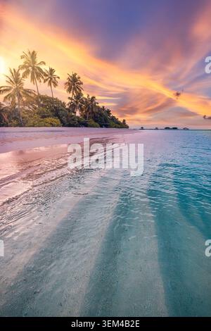 Colorful sunset beach vertical view, palm trees over white sand, dramatic golden clouds, turquoise sea washing tropical island shore, vivid evening Stock Photo