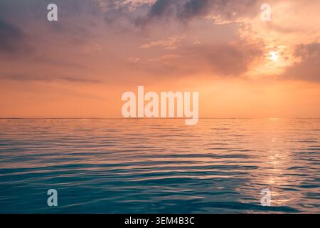 Dramatic orange sunset over calm ocean, glowing sun behind soft clouds, tranquil evening seascape reflection, warm twilight summer sky, peaceful coast Stock Photo