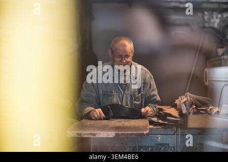 Senior shoemaker smiles while working in workshop Stock Photo