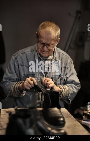 Elderly cobbler focused on repairing a leather boot Stock Photo