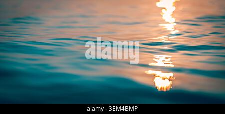 Moody twilight sun rays glint dark rippling water. Atmospheric ocean surface glowing reflection path. Deep blue evening seascape mysterious stillness Stock Photo