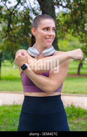 Sporty woman stretching arm across chest outdoors in park before fitness workout Stock Photo