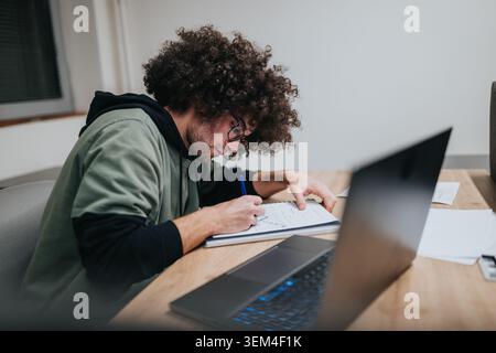Young man studying and taking notes at a laptop in a quiet modern workspace Stock Photo