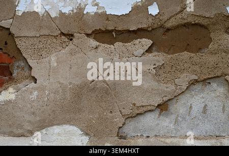 Horizontal close up of a deteriorating wall surface with cracked white paint, rough porous cement layers, exposed terra cotta colored layer, and red b Stock Photo