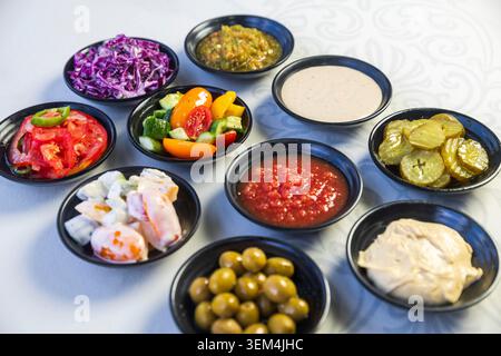Variety of traditional mezze appetizers, salads, and sauces served in small black bowls on a white table. Stock Photo