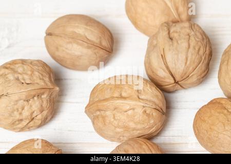 Top view horizontal closeup of whole raw walnuts in shell scattered on white wooden surface background texture Stock Photo