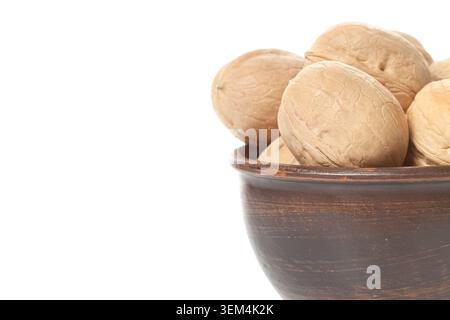 Side view horizontal closeup of whole raw walnuts in brown clay bowl accumulated in the corner on white copy space background Stock Photo