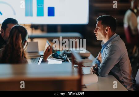 Business teammates discussing project data during a late-night meeting in a modern office Stock Photo