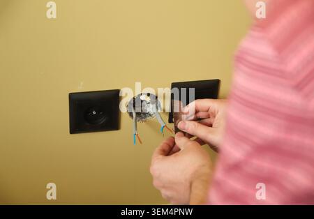 Close-up of electrician hands stripping electrical wires for socket installation. Electrician using utility knife blade to repair power outlet in a ye Stock Photo