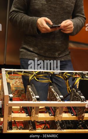Close-up of a man setup or maintaining a cryptocurrency mining rig with graphics cards. Businessman or miner using smartphone to monitor crypto farm s Stock Photo