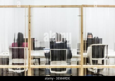 In a shared workspace, three people sit at desks focused on their computer screens. The transparent partitions provide a sense of privacy while mainta Stock Photo