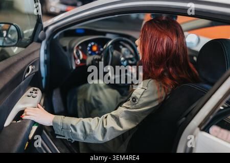 Red-haired woman sitting in the driver's seat with hand on car door controls Stock Photo