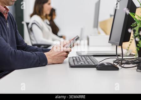 In a coworking space, individuals engage in tasks at their desks, using computers and mobile devices. Stock Photo