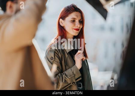 Young red-haired woman smiling with colleagues outdoors in an urban work setting Stock Photo