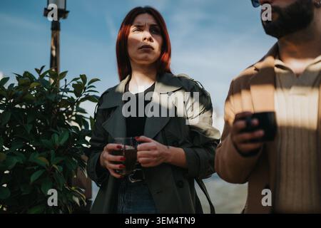 Two colleagues sharing a coffee break outdoors on a sunny urban terrace while talking quietly Stock Photo