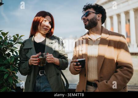 Work colleagues sharing coffee and laughing during an outdoor coffee break near a landmark Stock Photo