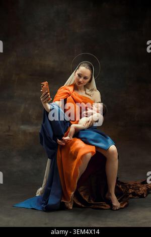 Smiling baroque mother taking selfie while holding baby in studio. Stock Photo