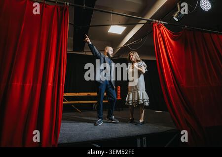 Young actors rehearsing dramatic scene on a small theater stage with red curtains and spotlight Stock Photo