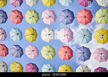 Colorful umbrellas suspended against a blue sky with clouds. A cheerful low-angle view of a vibrant urban street art installation. Stock Photo