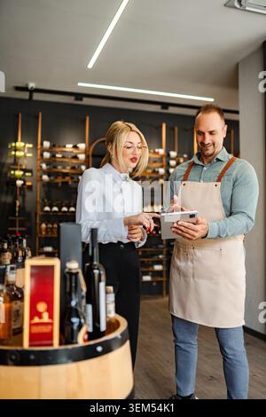 Shop assistant helping customer choosing wine on digital tablet Stock Photo