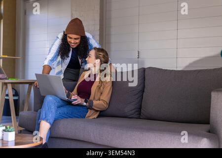 Diverse coworkers wearing casual clothes collaborating on laptop on sofa in lounge with succulent Stock Photo