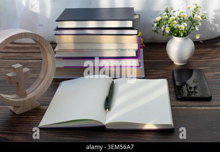 Christian Study Desk with Open Notebook, Books, Wooden Cross and Smartphone in Morning Light Stock Photo
